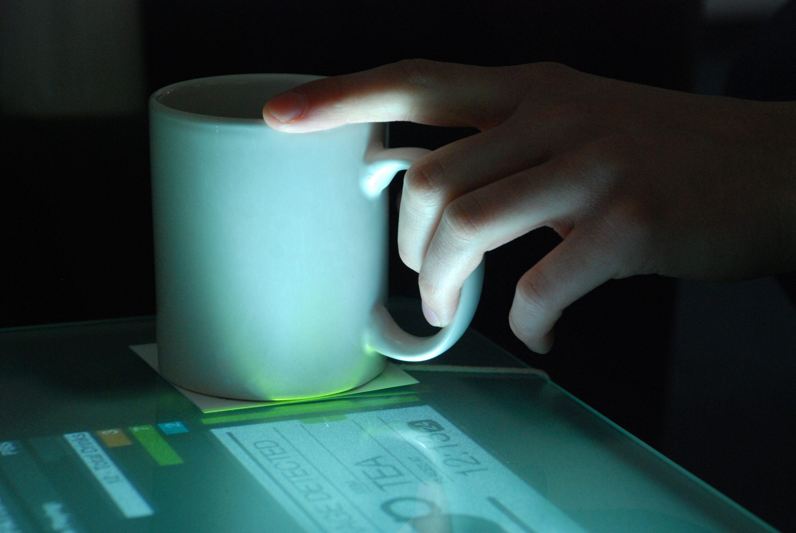 A hand placing a coffee cup on an illumated coffee table